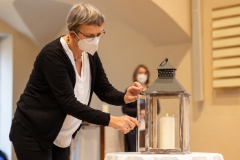 Frau mit Mund-Nasen-Schutz zündet eine Kerze an